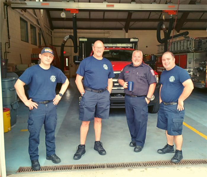 Four male firefighters pose for a photo infront of their truck.